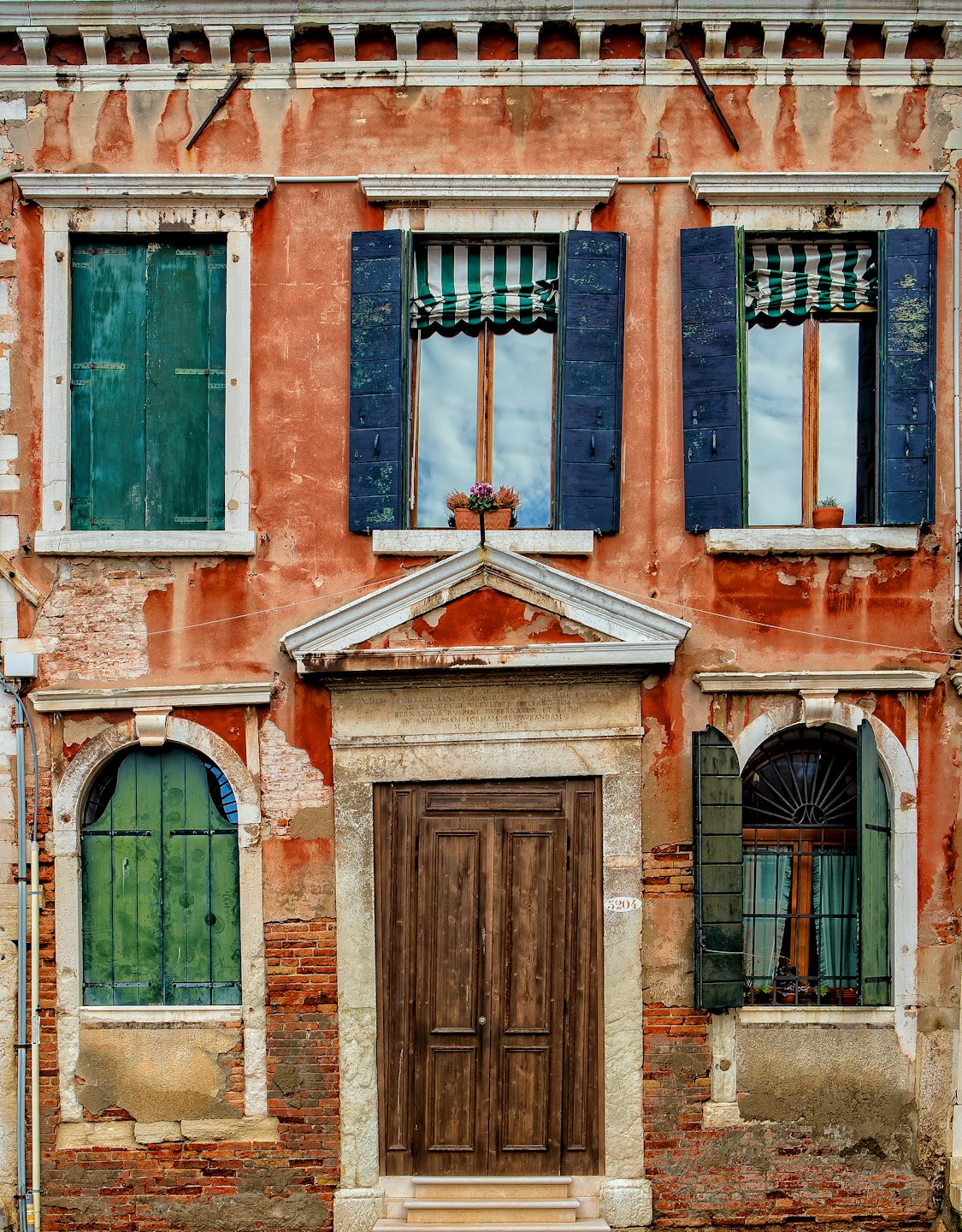 Verwitterte Hausfassade mit abblätternder Farbe und bunten Holzläden.
